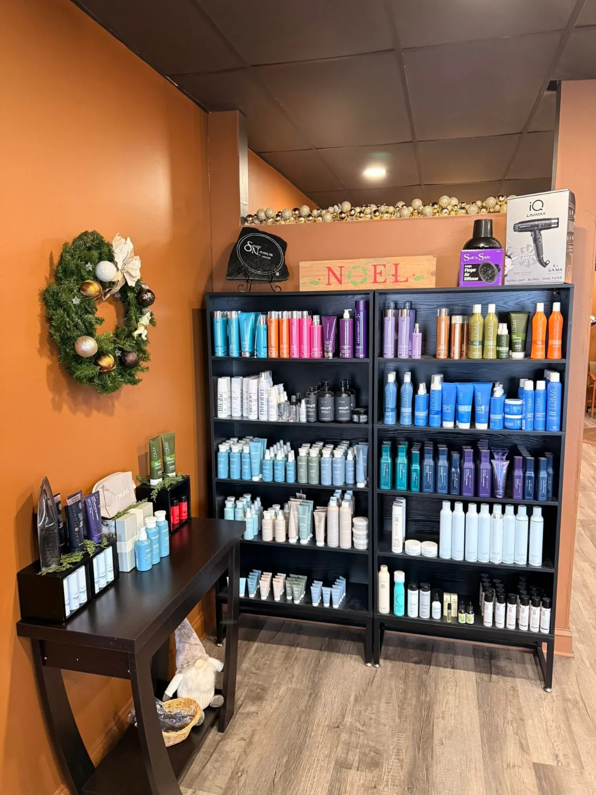 Two black bookcases of LOMA, Keratherapy, Neuma and Leaf + Flower hair products against an orange wall