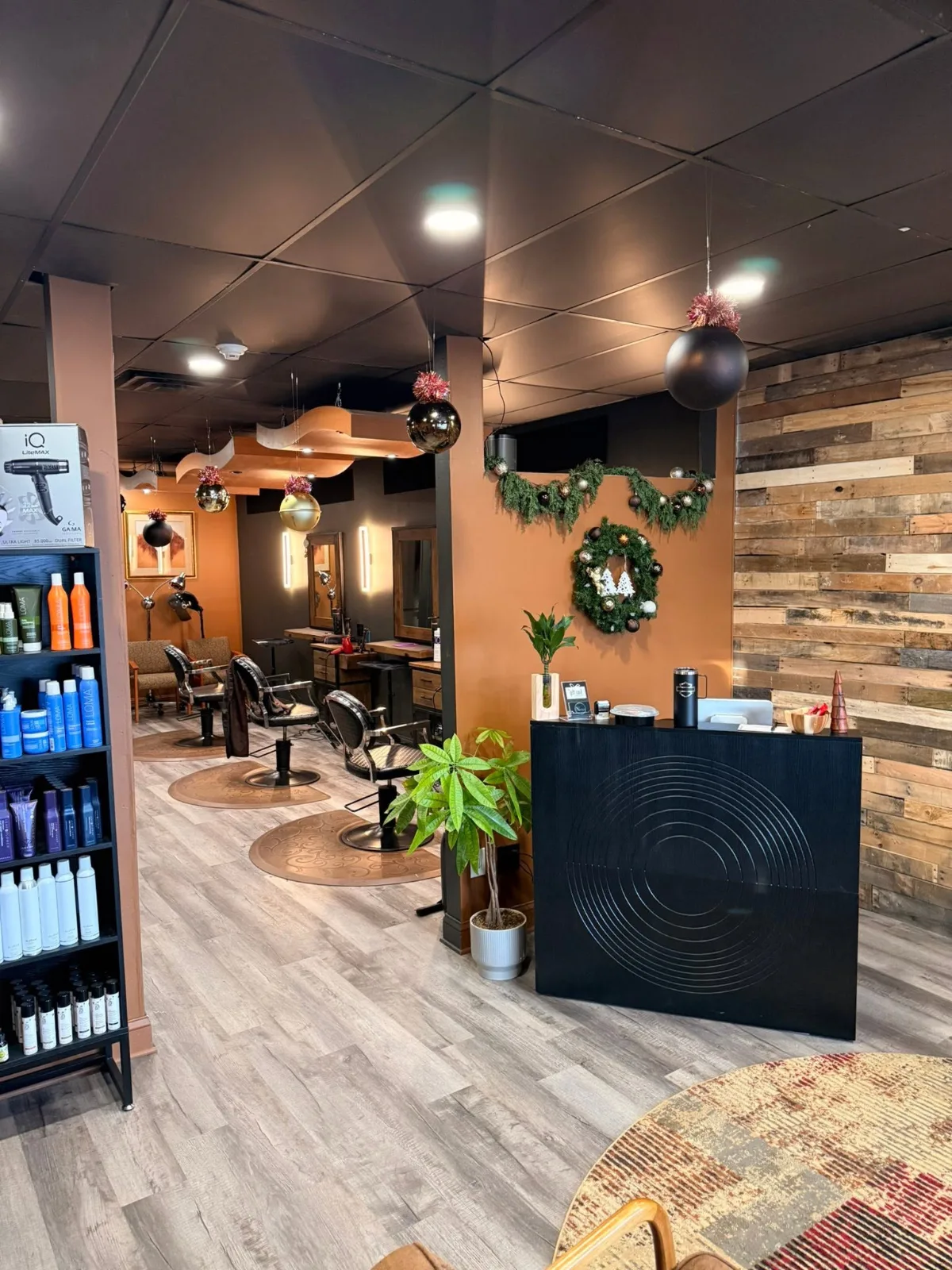 The salon floor: three styling chairs with wood-framed mirrors, a black front desk carved with circles, and a reclaimed-wood wall