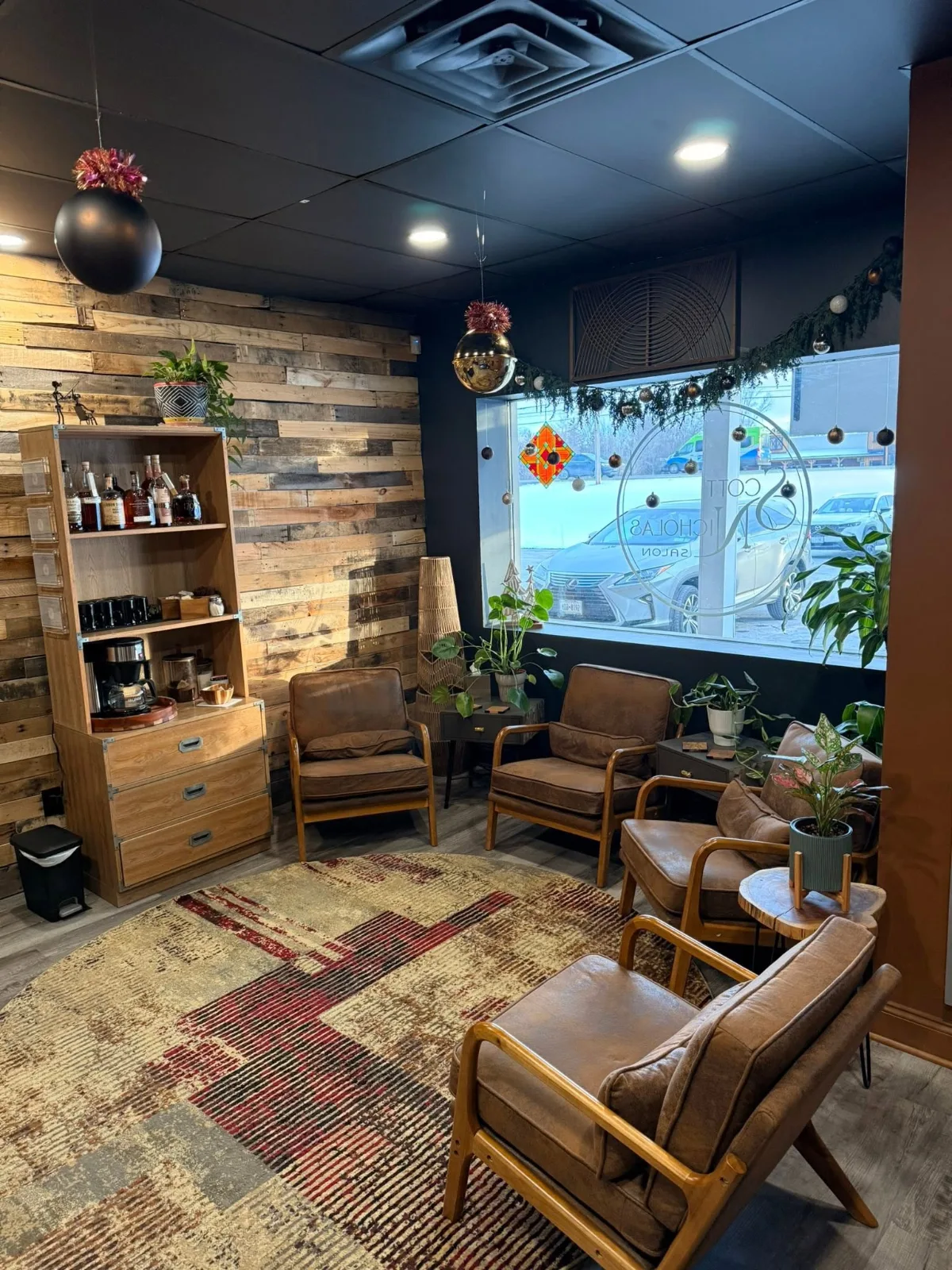 The lounge: brown leather armchairs on a round rug, a coffee bar against a reclaimed-wood wall, and the salon’s logo etched on the front window